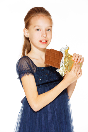 Beautiful blonde girl in a blue dress with curls eating a chocolateの写真素材