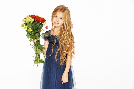 Charming little girl with curly hair in a blue dress with a bouquet of flowersの写真素材