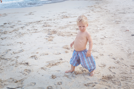 Toddler in a blue pants walking on a white sand in Thailandの写真素材