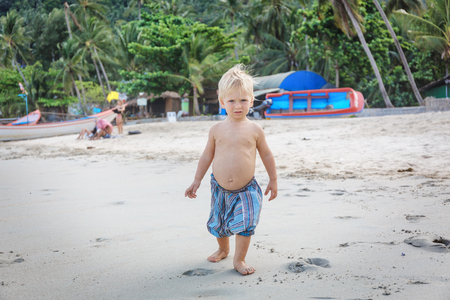 Little boy walking barefoot on white sand beachの写真素材