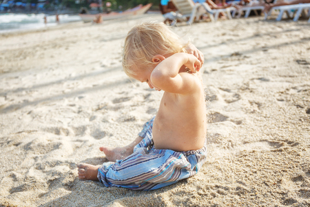 Baby with blond hair on the white sand beachの写真素材