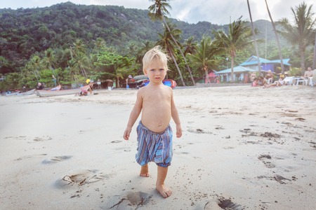 Little boy walking barefoot on white sand beachの写真素材