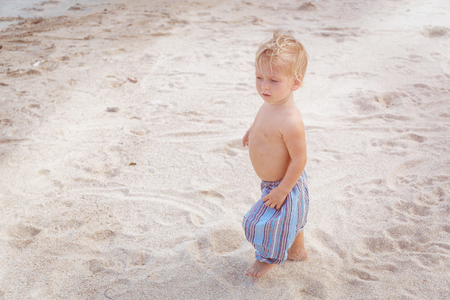 Toddler in a blue pants walking on a white sand in Thailandの写真素材