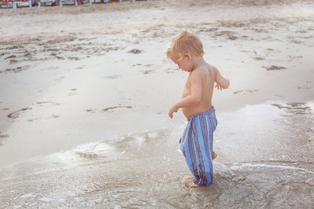 Toddler in a blue pants walking on a white sand in Thailandの写真素材