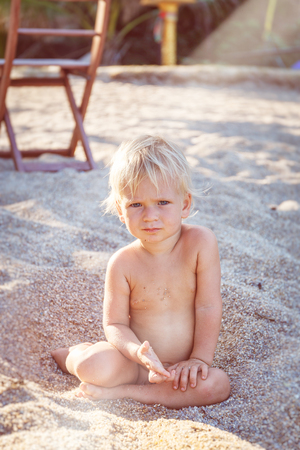 Little boy with blue eyes and white hair sitting on white sand and look up at the cameraの写真素材