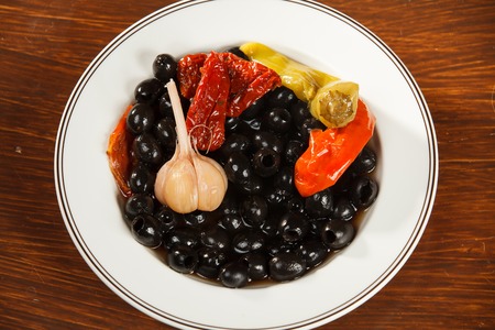 Plate of olives, marinated peppers and garlic on a wooden tableの写真素材