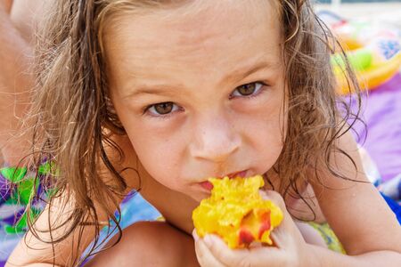 Cute boy eating a peach on the beachの写真素材
