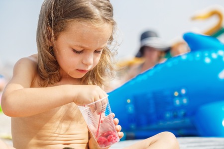 Beautiful boy is eating raspberries on the beachの写真素材