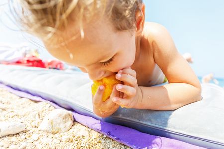 Cute boy eating a peach on the beachの写真素材