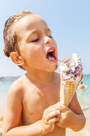 Beautiful boy is eating an ice cream on the beachの写真素材