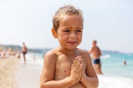 Sweet little boy with hands in namaste on the beachの写真素材