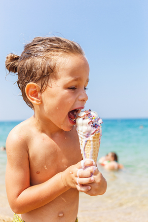 Beautiful boy is eating an ice cream on the beachの写真素材