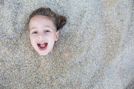 Boy hidden in the sand on the beachの写真素材