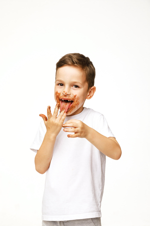 little boy with face and hands in chocolate on a white backgroundの写真素材