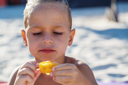 Child boy is eating fruits on the beachの写真素材