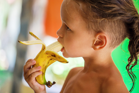 Child boy is eating fruits on the beachの写真素材