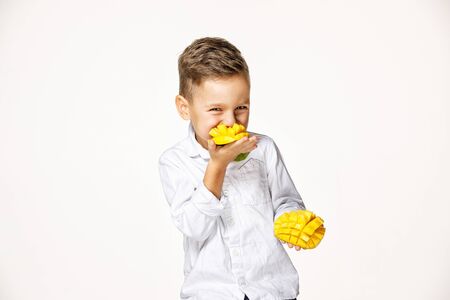 handsome boy in a white shirt is eating a mangoの写真素材