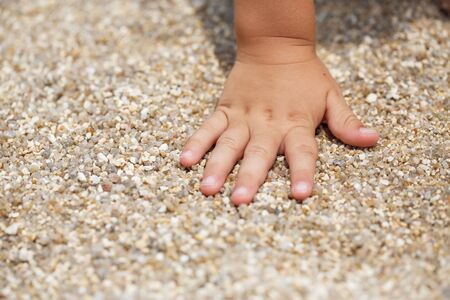 Baby small hand touching brown sand in Thailandの写真素材