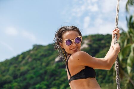beautiful woman in a black swimsuit on a beach swingの写真素材