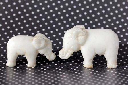 Side view of two small ancient marble Toy Elephants against black and white Polka Dot background (white polka dots on a black background)の写真素材