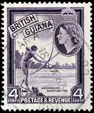 BRITISH GUIANA - CIRCA 1954: A stamp printed by BRITISH GUIANA shows Native American shooting fish, circa 1954のeditorial素材