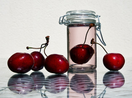 Wild cherries and glass jar of sweet cold compote against a high key background with space for your text. Selective and soft focus.の写真素材
