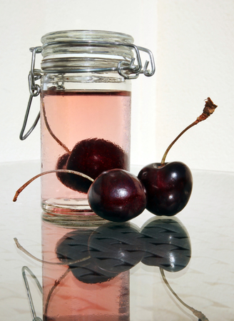 Wild cherries and small glass jar of sweet cold compote against a high key background. Selective and soft focus.の写真素材