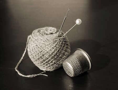 Still life with vintage thimble, thread, pin and sewing needle in sepia tone against a low key...
