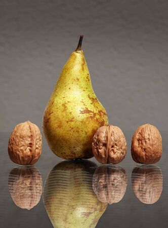 Still life with sweet ripe pear and three walnuts in their nutshells