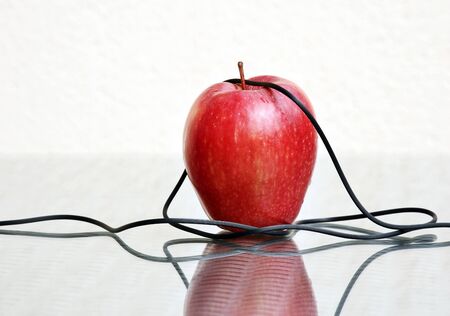 Red ripe apple and thin electrical headphones wire against a high key background with amazing reflections. Selective and soft focus and space for your text.の写真素材