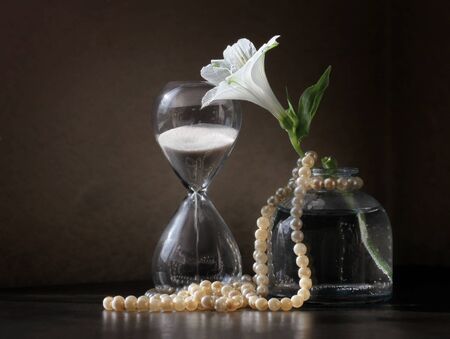Retro style still life with vintage sandglass, Alstroemeria flower in the small bottle and string of...