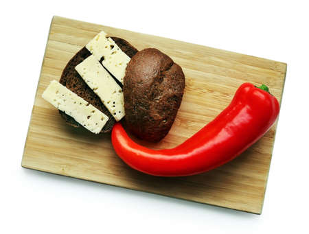 Still life with red Ramiro pepper, brown bread and cheese slices on the wooden cutting board against...