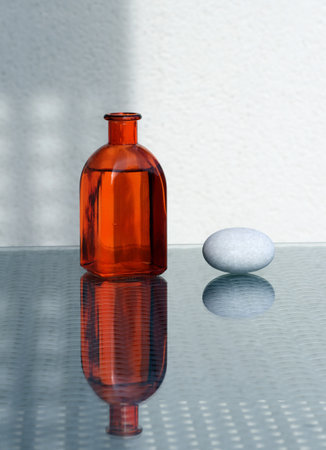 Abstract minimalist still life with vintage bottle of colored glass with aromatic oil and sea pebble. Beautiful reflections and shadows. Free space for your text.の写真素材