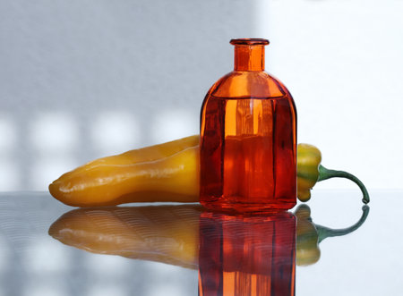 Still life with sweet long pepper and glass colored bottle with amazing reflections against a high key background. Shallow depth, selective focus. Free space for your text.の写真素材