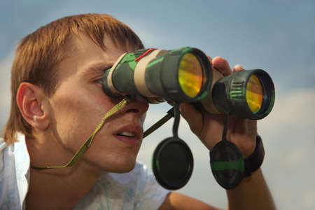 The young man looks at the removed subjects through the field-glass.の写真素材