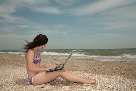 Girl works on laptop and sunbathes on a beach.の写真素材