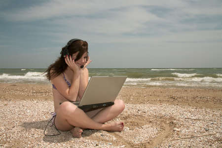 Girl works on laptop and sunbathes on a beach.の写真素材