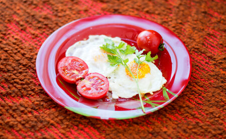 Fried eggs with vegetables on a red plate against a red rugの写真素材