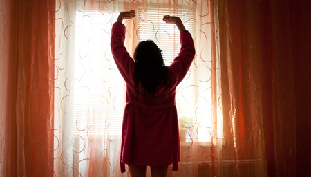 The woman to stretch in the morning near the window closed by curtainsの写真素材