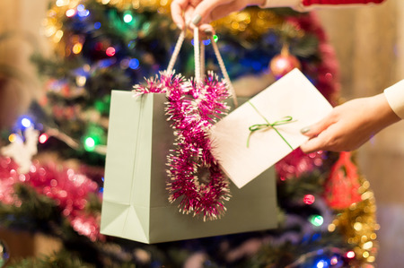 Gift bags and envelopes in a female hand with Christmas tree with ornamentsの写真素材