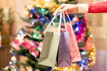 Gift bags in a female hand with Christmas tree with ornamentsの写真素材