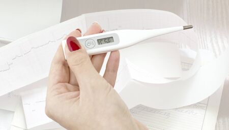 Electronic thermometer in the women's hands on the background paper ECG