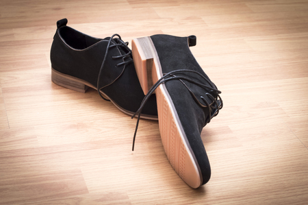 Black suede shoes with laces on a background of wooden parquetの写真素材