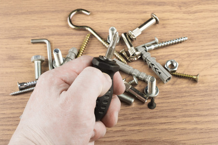 Screwdriver in the hand of the master on the background of various bolts and dowels for mounting and fasteningの写真素材