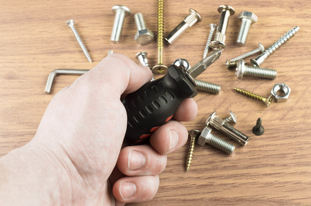 Screwdriver in the hand of the master on the background of various bolts and dowels for mounting and fasteningの写真素材