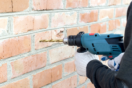 The process of drilling using electric drills on a background of a brick wallの写真素材
