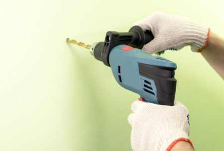 The process of drilling using electric drills on a background of green wallの写真素材