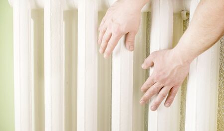 Touching hands to sections of cast iron radiator of white colorの写真素材