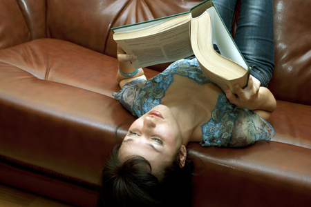 The woman with the book lying in a room on a sofaの写真素材