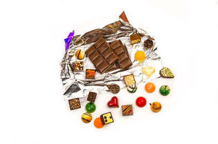 Tile of milk chocolate in a foil wrap and various chocolate candies on a white backgroundの写真素材